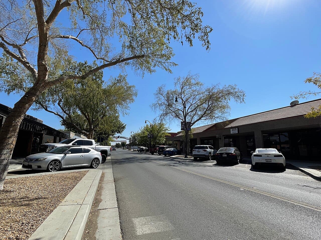 Tree-lined downtown Coalinga street with storefronts, parked cars, and a welcome arch in the distance.