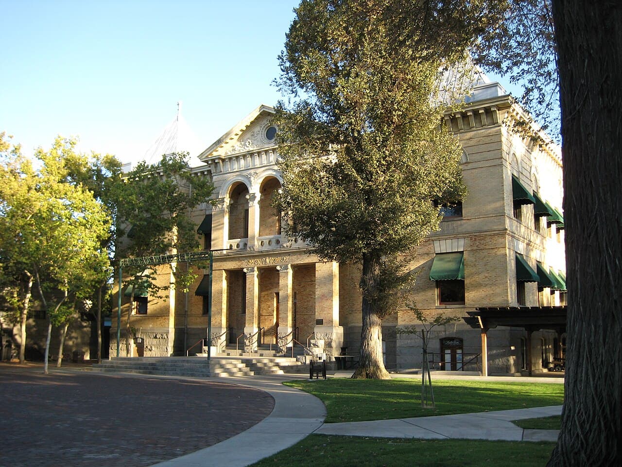 The brick facade and arched entrance of the historic Kings County Courthouse in Hanford, framed by trees and lawn.