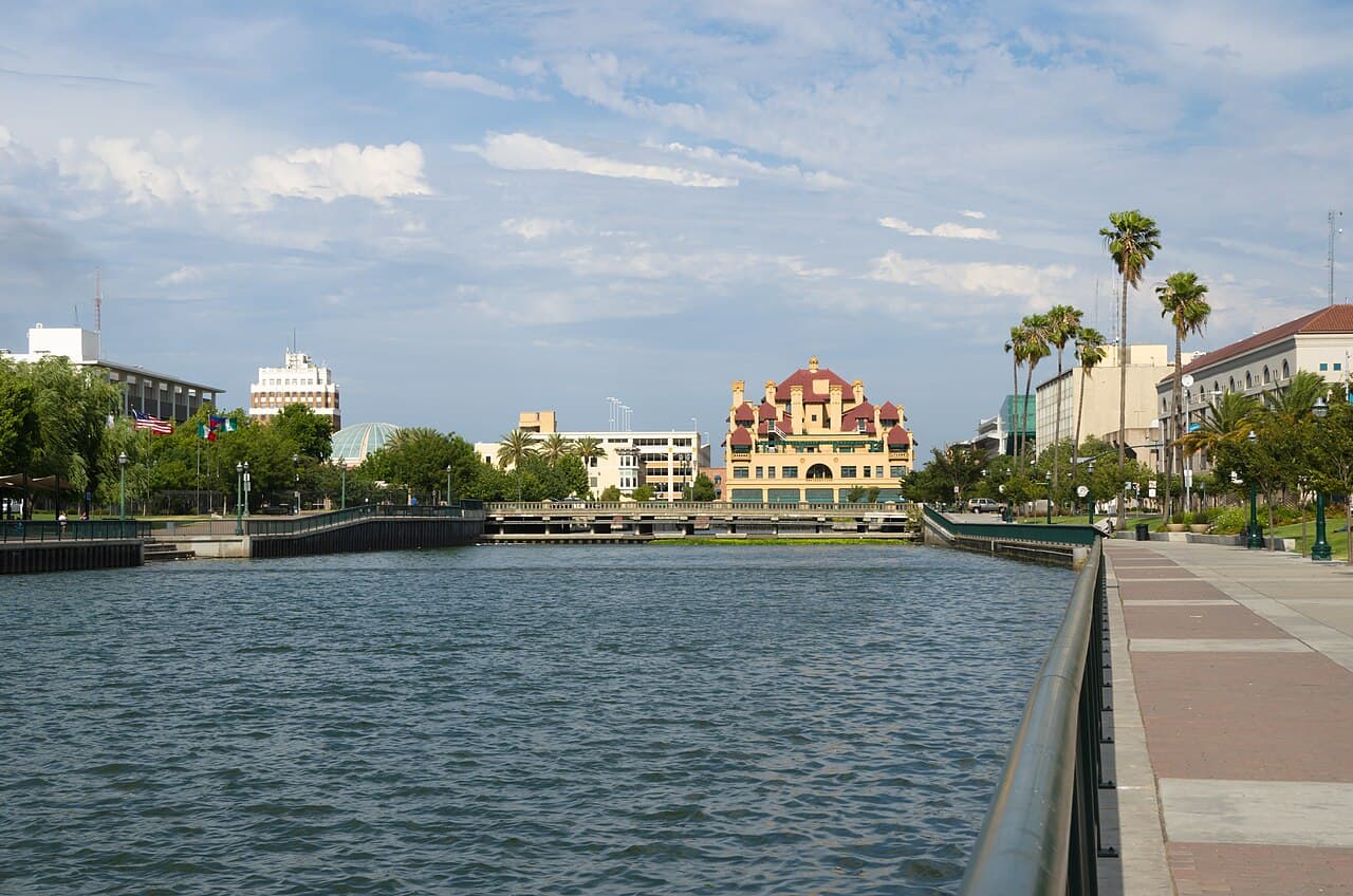 Downtown Stockton buildings and a palm-lined promenade beside the Stockton Channel.