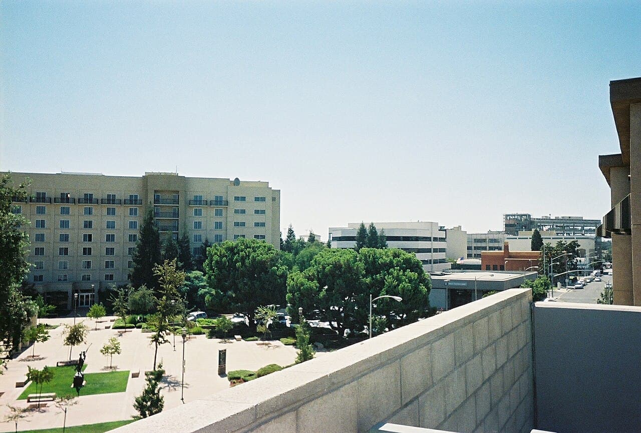 Downtown Visalia buildings beside a tree-lined plaza and a street extending through the city center.